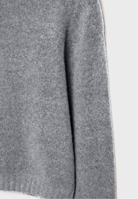 Pull en laine grise présentant une texture douce, une coupe carrée et un ourlet côtelé. Le matériau semble légèrement duveteux, renforçant son aspect confortable.