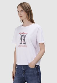 T-shirt en coton blanc avec un graphisme de bottes de cowboy et le texte "Champion du Monde de Rodeo" en rouge. Coupe décontractée avec des manches courtes.