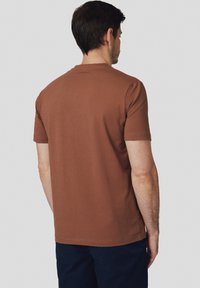 Brązowa bawełniana koszulka z krótkim rękawem, okrągłym dekoltem i gładkim tyłem. Posiada minimalistyczne detale szycia w okolicy kołnierza.