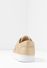 Sneaker in suede oro con ritagli decorativi, suola in gomma bianca, colletto imbottito e dettagli con logo sul lato.