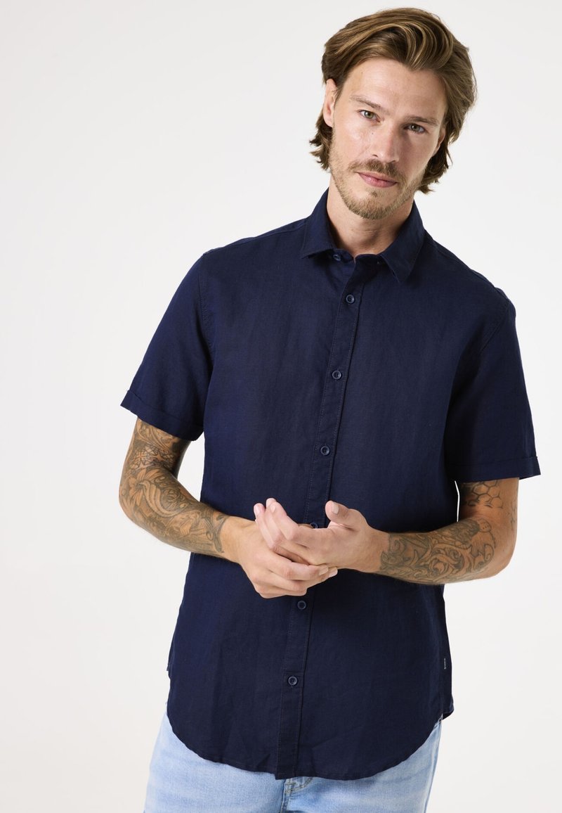 Korte mouwen marineblauw linnen overhemd met een button-down kraag, voorzien van knopen aan de voorkant en een gebogen zoom, gedragen door een persoon met tatoeages.