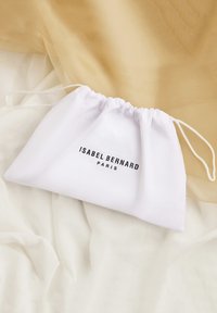 Weißer Zugbeutel aus glattem Stoff, mit schwarzem Text "ISABEL BERNARD PARIS", der deutlich auf der Vorderseite zu sehen ist.