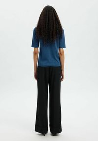 Sininen neulepaita lyhyillä hihoilla, suora helma, yhdistettynä korkeavyötäröisiin mustiin leveälahkeisiin housuihin, joissa on käännetyt lahkeet.