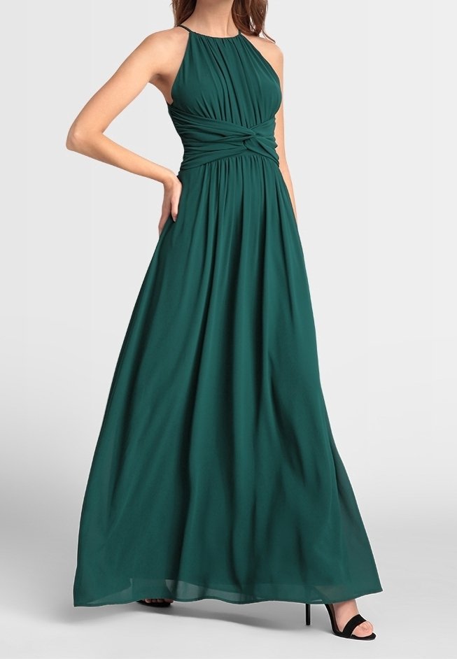 Robe longue sans manches vert foncé avec corsage froncé et détail torsadé à la taille, portée avec des talons hauts noirs ouverts.