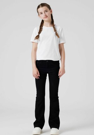 Schwarze weit geschnittene Jeans, tailliert mit Vordertaschen. Kombiniert mit einem schlichten weißen T-Shirt. Weiße Sneaker runden das Outfit ab.