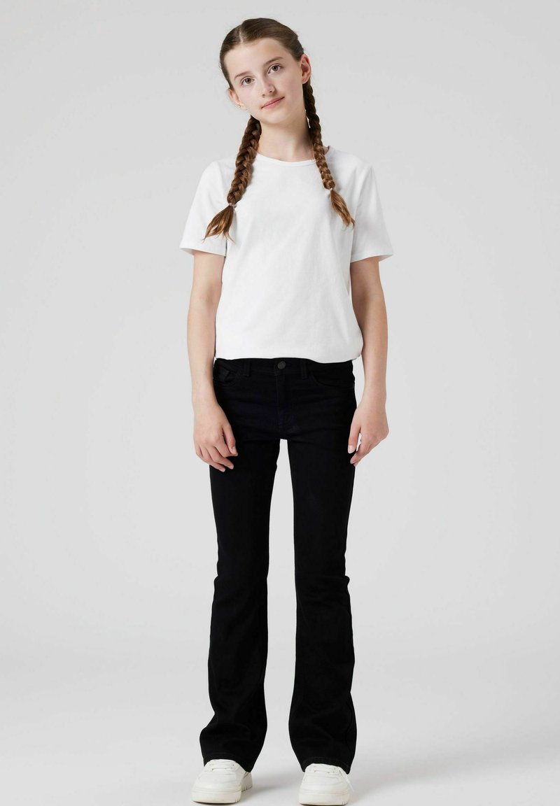 Schwarze weit geschnittene Jeans, tailliert mit Vordertaschen. Kombiniert mit einem schlichten weißen T-Shirt. Weiße Sneaker runden das Outfit ab.