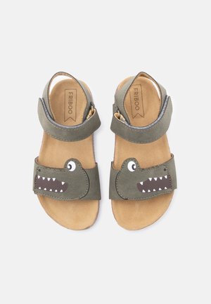 Sandales ouvertes pour enfants avec des sangles vertes ornées de visages de crocodile dessinés avec des yeux et des dents, et des semelles intérieures beiges rembourrées portant l'inscription "FRIBOO".