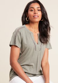 Olijfgroen T-shirt met korte mouwen en een V-hals, versierd met kantdetails op de schouders. Zachte stof met een ontspannen pasvorm.