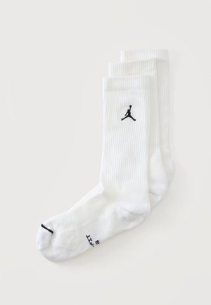 Tre par hvide crew-sokker med et sort Jumpman-logo og en sort tåstribe på en tå mod en ensfarvet baggrund.