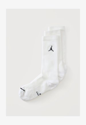 Trois paires de chaussettes blanches montantes avec un logo Jumpman noir et une bande noire sur un orteil, sur un fond uni.