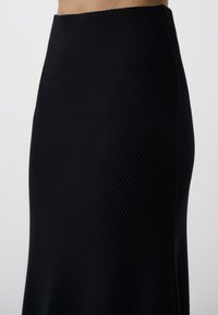 Jupe noire côtelée avec une silhouette ajustée, présentant une texture lisse et une taille élastique, s'évasant vers l'ourlet.