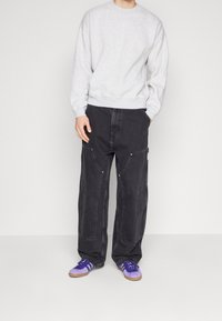 Sweatshirt en coton gris avec un col rond classique, associé à un pantalon cargo en denim noir ample avec poches et accents en laiton. Baskets violettes.