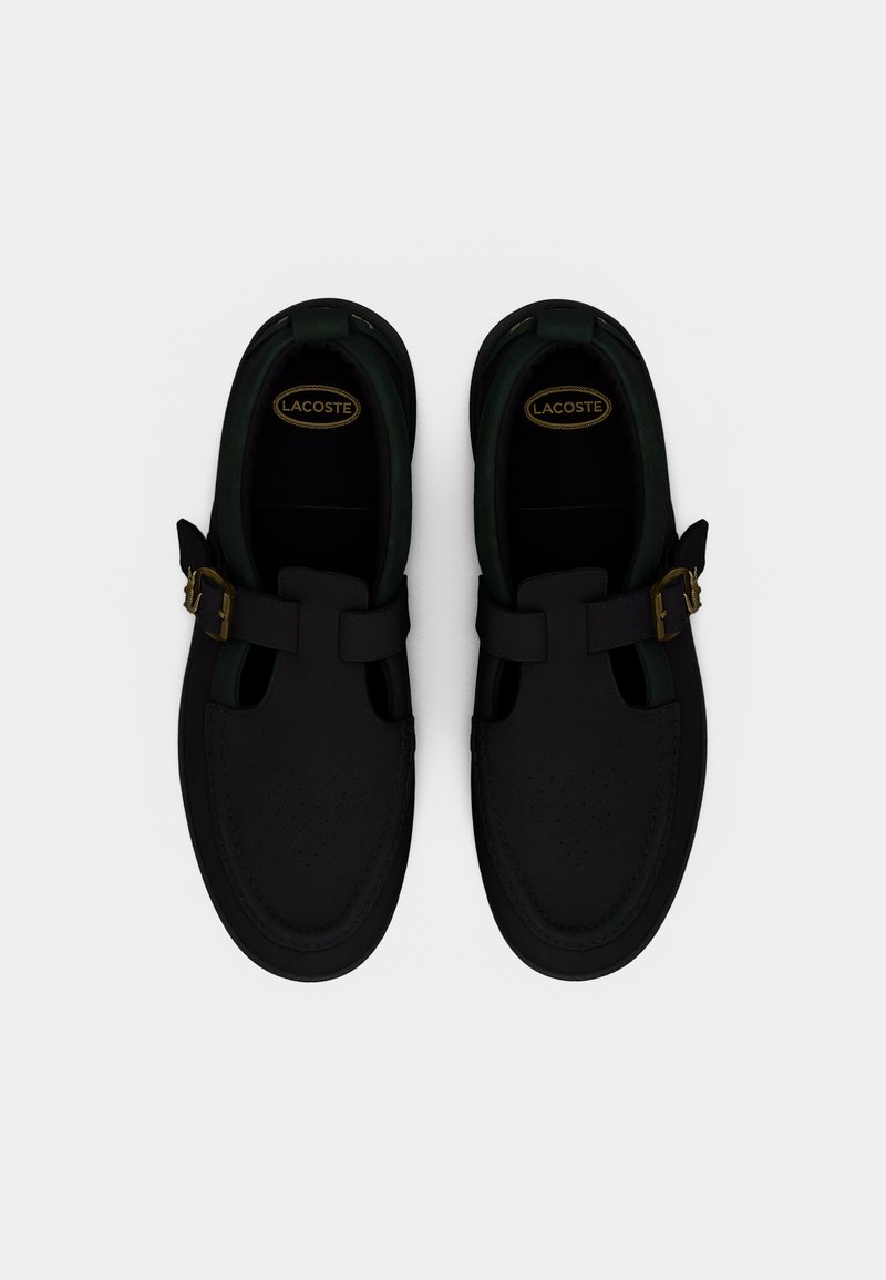 Scarpe nere con finitura liscia, caratterizzate da una fibbia a cinturino, dettagli ritagliati e punta tonda. Foderate in verde scuro con accenti traforati.