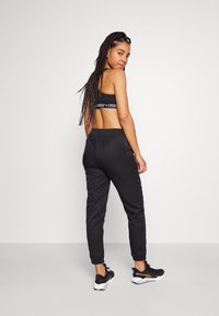 Pantaloni sportivi neri con una vestibilità tapered, vita elastica e tasche laterali, abbinati a un reggiseno sportivo nero coordinato con dettagli del logo.