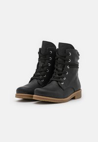 Bottines en cuir noir avec bout rond, devant à lacets et œillets en argent. Présente une semelle extérieure brune texturée pour une meilleure adhérence.