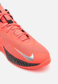 Chaussure de basketball Nike en corail vif avec tige en maille texturée, accents noirs, logo swoosh argenté et semelle en caoutchouc avec motifs de semelle.