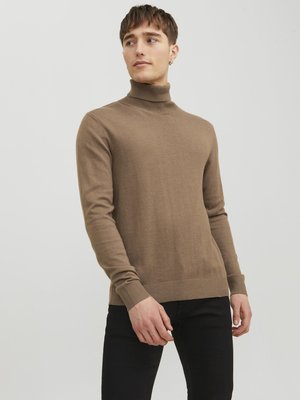 Maglione a collo alto marrone in un tessuto morbido e liscio, con maniche lunghe e polsini a coste. Indossato con pantaloni neri, presenta una silhouette aderente.