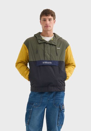 Giacca antivento leggera a blocchi di colore con pannelli verdi, gialli e blu scuro. Presenta un cappuccio regolabile, tasca frontale e orlo con cordino.