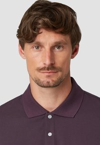 Heren polo-shirt in donkerpaars, met een kraag, een drievoudige knoopsluiting en een gestructureerde stof. Gladde oppervlakte met minimale details.