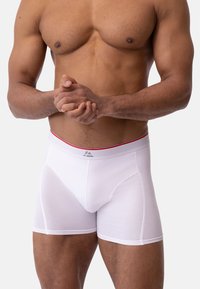 Bílé boxerky s těsným střihem, se švem zvýrazněným červenou a hladkou texturou. Materiál působí měkce a pružně.