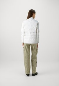 Doudoune blanche avec un design matelassé, col montant et manches longues, associée à un pantalon cargo vert olive et des chaussures noires.