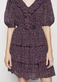 Robe fleurie violet foncé avec volants superposés, manches courtes bouffantes et encolure en V avec détails de volants à l'avant.