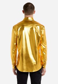 Kuldmetallist pikkade varrukatega särk, mille pinnal on sile ja läikiv tekstuur. Omab klassikalist kraed ja nööpidega mansette, ning kaardus hemline'i.