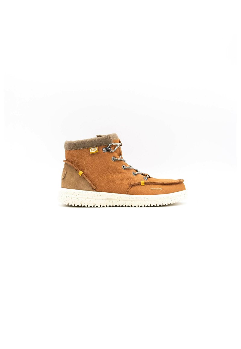 Botas de tobillo de cuero marrón con un suave cuello de forro de lana color canela, suela moteada de blanco y ojales de metal plateado para los cordones.