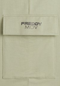 Fascia di tessuto verde chiaro con il logo "FREDDY MOV" in caratteri scuri, caratterizzata da una texture liscia e bordi cuciti.