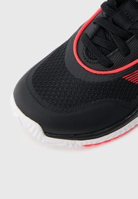 Zwart sportschoen met een bovenwerk van mesh, rode accenten en een gestructureerde rubberen zool. Ronde neus en vetersysteem voor een stevige pasvorm.