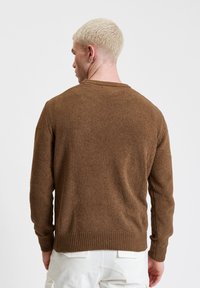 Brązowy sweter dzianinowy o teksturowanym wykończeniu, z okrągłym dekoltem i ściągaczami. Tył jest gładki, podkreślający bogaty kolor swetra.