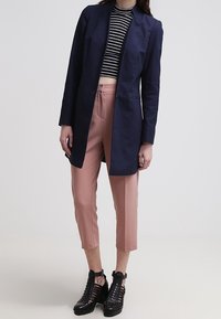 Blazer largo azul marino sobre una camiseta tipo crop blanco y negro a rayas, combinado con pantalones recortados rosa claro y botines negros con tiras al tobillo.