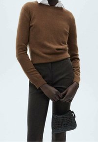 Pull en laine marron avec un col rond, associé à un pantalon sombre. Tient un petit sac à main noir texturé présentant un motif crocodile.