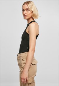 Svart ermeløs topp med tettsittende design, glatt tekstur, kombinert med beige cargo bukser med lommer og knappeåpning.