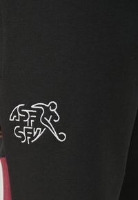 Pantaloni sportivi neri con design aderente. Presentano un logo ricamato bianco che raffigura una figura che corre sul lato sinistro inferiore.