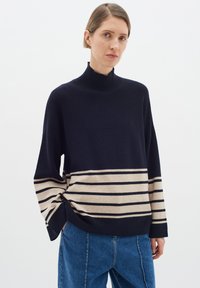 Pulover dungat cu navy și bej, cu guler înalt și umeri lăsați, realizat dintr-un material moale. Asortat cu blugi blue largi.