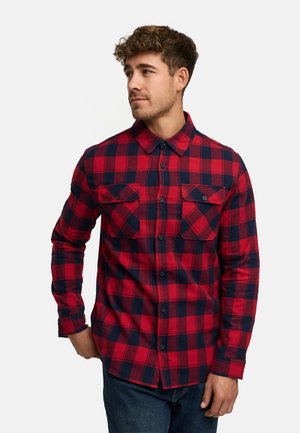 Camisa de franela a cuadros en rojo y marino con dos solapas en los bolsillos, mangas largas, cuello abotonado y tela texturizada.