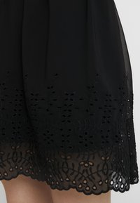 Svart klänning med intrikata blommönster vid fållen, med ett genomskinligt överlägg och vågkant, i ett lätt material.