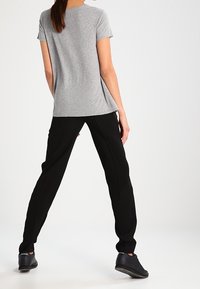 Szary t-shirt z krótkim rękawem w połączeniu z czarnymi zwężanymi spodniami. Materiał wydaje się miękki; spodnie mają luźny krój z bocznymi akcentami. Czarne trampki.