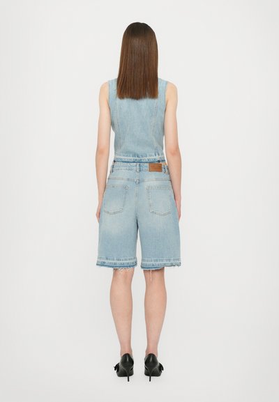 Denim kombinezon u svijetloplavoj boji s pripijenim bezrukavnim gornjim dijelom i opuštenim šortsevima. Ima obrubljene rubove i stražnje džepove, uparen s crnim potpeticama.