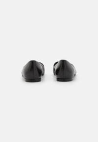 Ballerine in pelle nera con una finitura liscia, punta arrotondata e tacco basso. Il design presenta cuciture minime e una silhouette elegante.