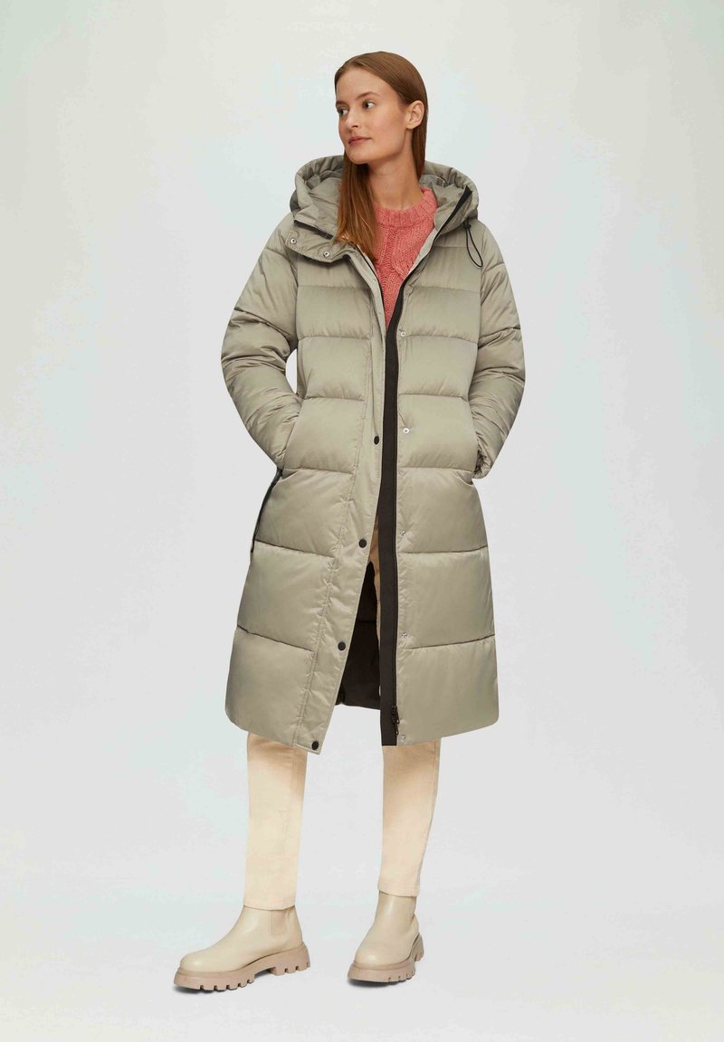 Langer, hellgrauer Puffer-Mantel mit Kapuze, ausgestattet mit Druckknöpfen und seitlichen Taschen, kombiniert mit einem pinken Pullover und beigen Ankle Boots.