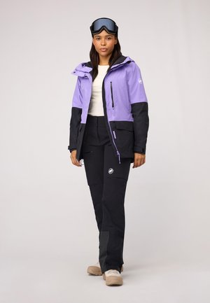 Lila und schwarze Skijacke mit verstellbarer Kapuze und mehreren Taschen, kombiniert mit schwarzen Hosen, die ein Logo und strukturierte Paneelakzente aufweisen.