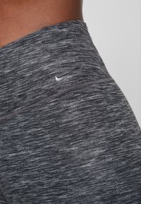 Leggings high-waisted Nike in un motivo testurizzato nero e grigio mélange con un piccolo logo bianco nella parte superiore sinistra.