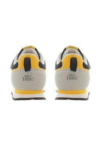 Zadní pohled na šedé a žluté tenisky s černými akcenty, texturovanou látkou a logem "SINCE 1890" na patě. Design gumové podrážky.
