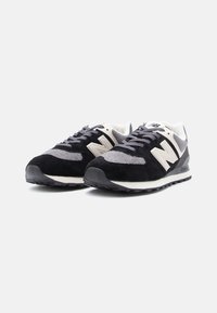 Pár čiernych a šedých tenisiek New Balance s bielym logom a šedými šnúrkami, naklonené tak, aby ukázali predný a bočný pohľad na bielom pozadí.
