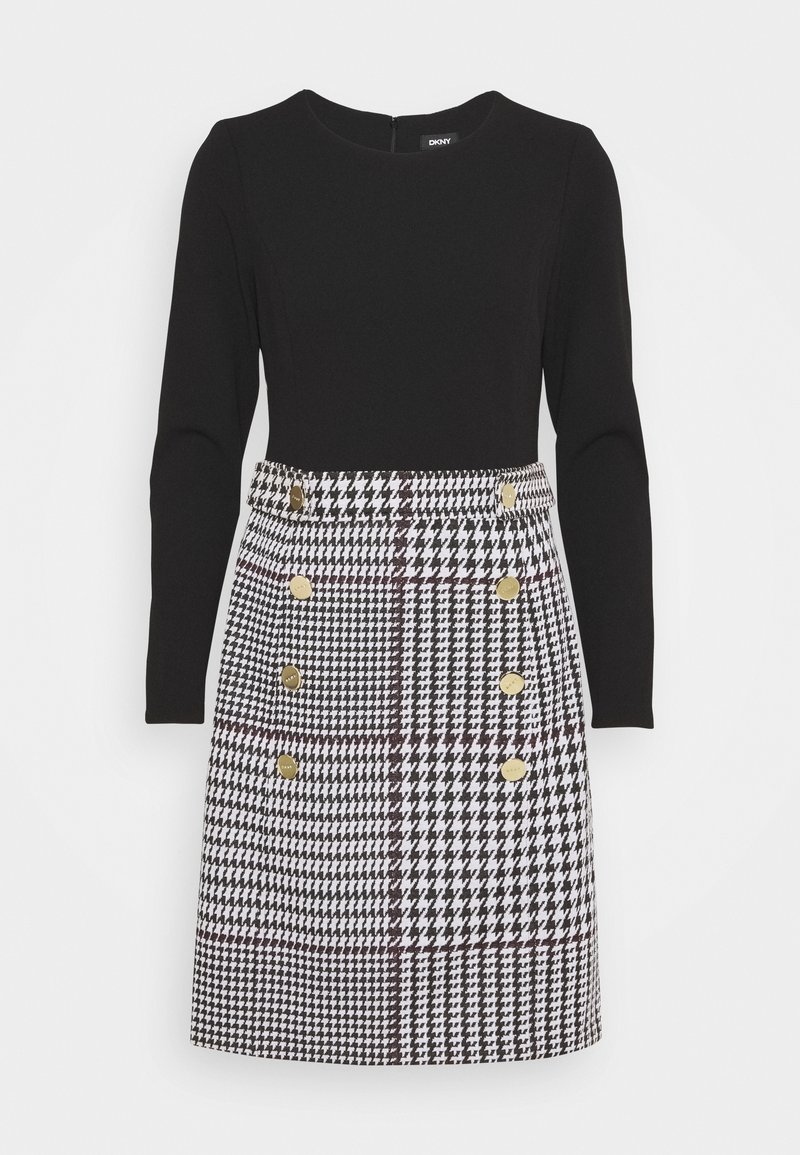 Haut noir à manches longues avec jupe pied-de-poule noir et blanc attachée, présentant une double rangée de boutons dorés à l'avant.