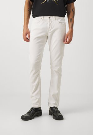 Jeans in denim bianco con una vestibilità slim, dotati di chiusura a bottoni e cerniera, design a cinque tasche e una texture sottile, abbinati a scarpe nere.