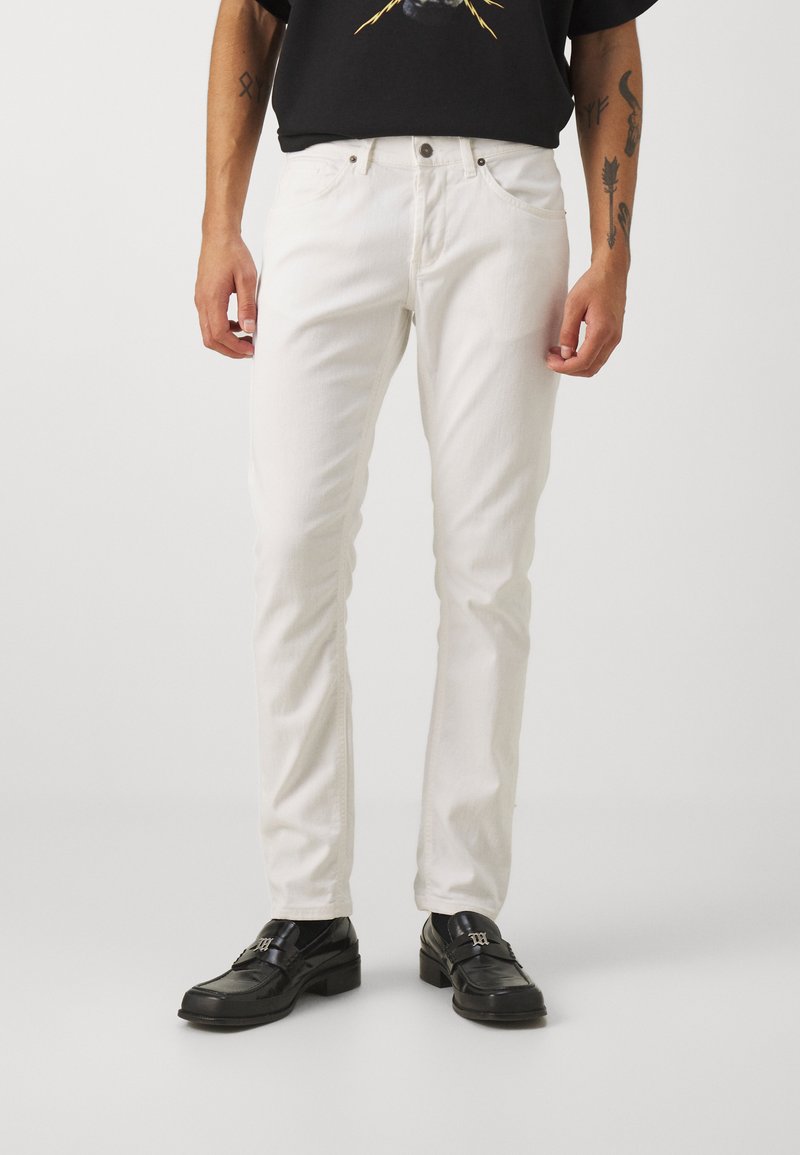 Jeans in denim bianco con una vestibilità slim, dotati di chiusura a bottoni e cerniera, design a cinque tasche e una texture sottile, abbinati a scarpe nere.