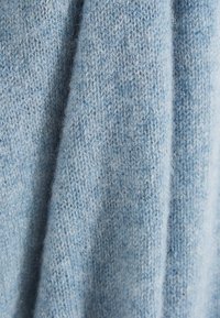 Tissu en maille texturée bleu clair avec une apparence douce et duveteuse. Le matériau présente des côtes et des teintes variées pour une profondeur subtile.